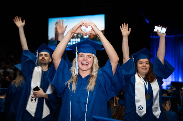  Recent college graduates raise their arms and make a heart hand symbol during commencement. 