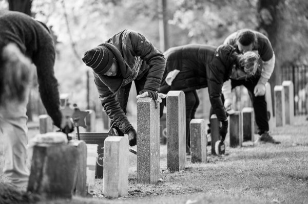  People are bending over scrubbing on a line of old headstones at a cemetery.