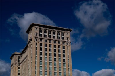 A large building is set against a blue sky with some clouds.