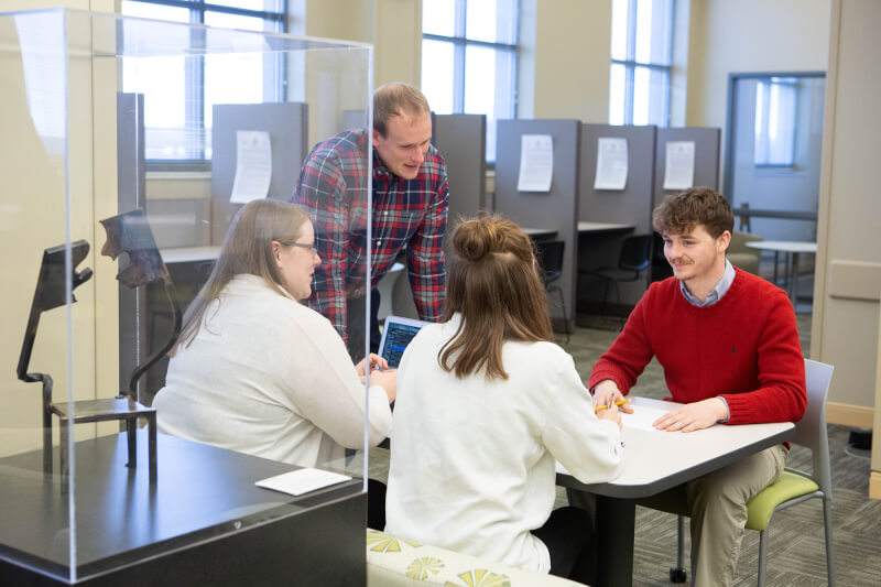 Man chatting with students at table.