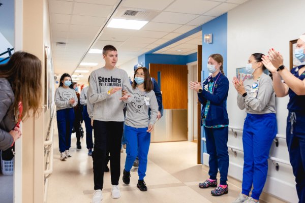 staff in scrubs and masks line a hallway to applaud Sam Smalldon, as he is helped down the hall