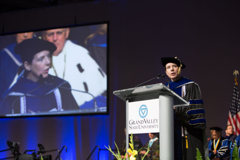 woman in regalia speaking on stage 