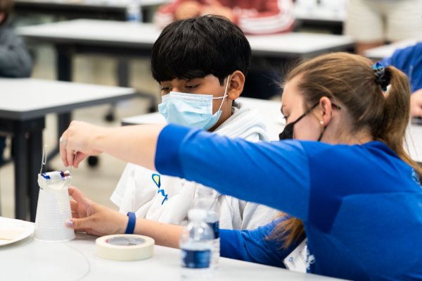 Instructor and camper build motor at a table, wearing masks