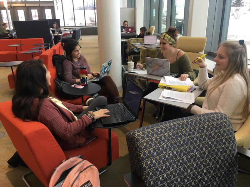 four students in chairs, with computers, papers