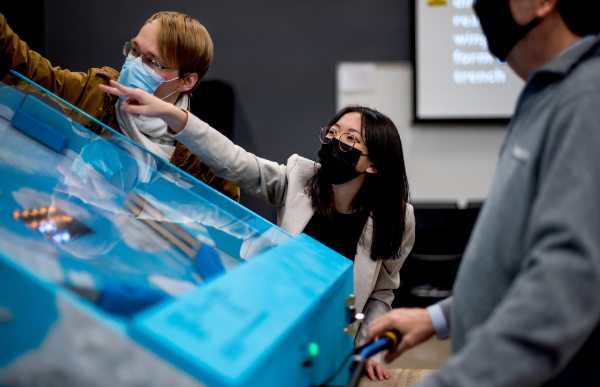 three students watching a can travel up a makeshift pinball machine