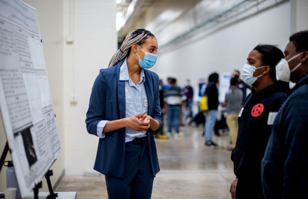 student stands by poster display, talking with two high school students