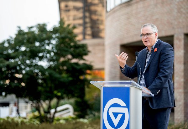 A person gestures with the hand while speaking at a podium with the Grand Valley logo.