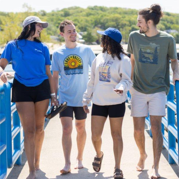 Four students wearing new Lake + Valley clothing items walk along the beach, laughing and talking together.