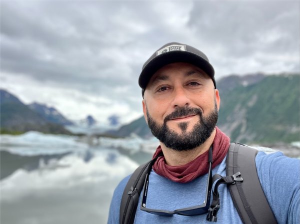 A person wearing a hat poses for a photo in front of mountains.