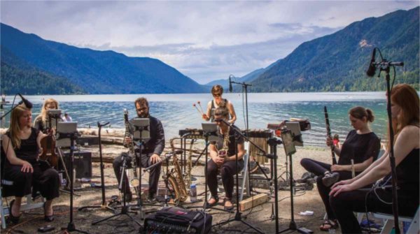 Musicians perform with mountains and a body of water behind them.