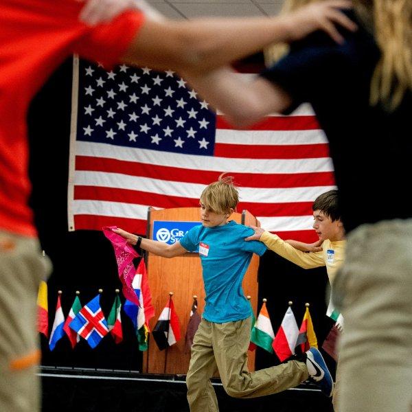 sixth graders dancing in a circle, American flag in background, small country flags on display also