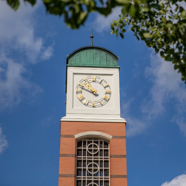The top of the carillon tower is set against blue sky and wispy clouds with some green tree leaves in the foreground.