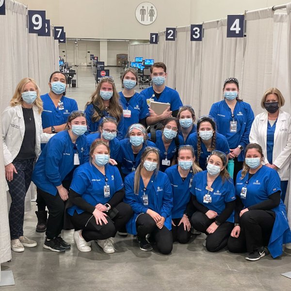 Kirkhof College of Nursing faculty members, in white lab coats, and students in blue scrub shirts, are pictured at the vaccine clinic in Grand Rapids.