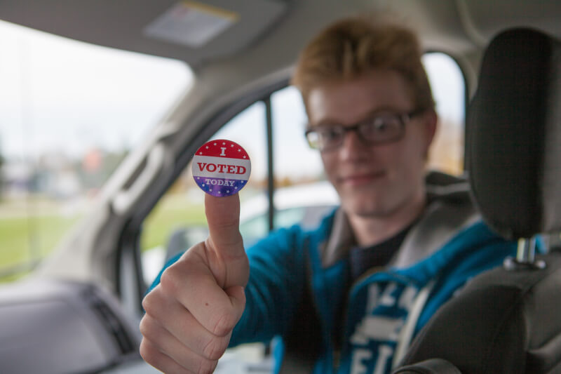 A photo of a student holding up a "I Voted" sticker.