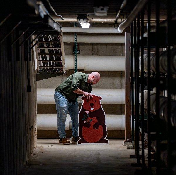 A man positions a cardboard cutout of a groundhog at the end of a dark tunnel.
