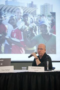 Steve Lyon, baseball coach, talks about the team's trip to Cuba. In the photo behind him, catcher Jared Cowan poses with Cuban youth.