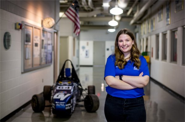 Annika Mattson stands with arms crossed next to the Laker Racing car in a hallway