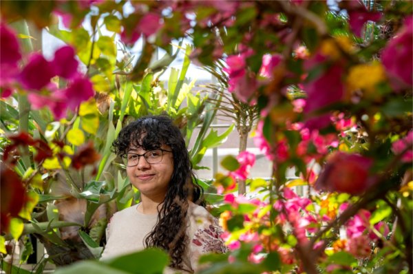 Daylona Jackson framed by blooming pink flowers in a greenhouse