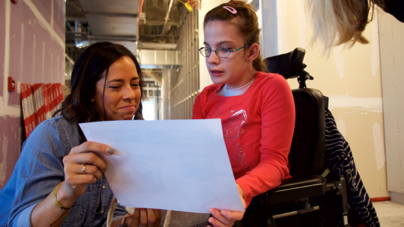  Student smiling while showing a young girl in a wheelchair a photo