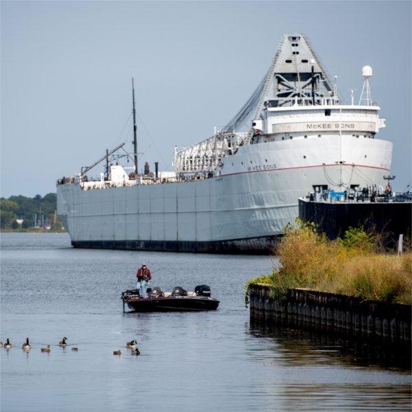 A man in a boat fishes in front of a freighter on Muskegon Lake.