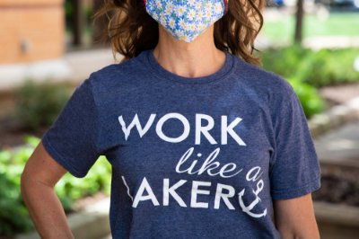 A profile of a woman from the nose down, showing a face covering and blue t-shirt that reads&#x3a; work like a Laker.