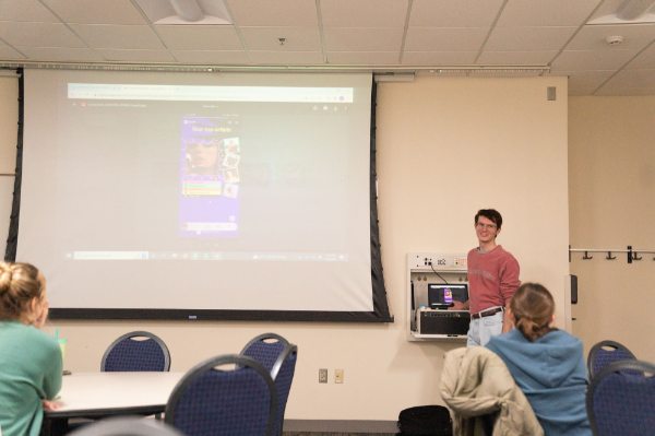 Caleb White stands to the left of a projection screen that shows a phone Spotify listing of Taylor Swift.
