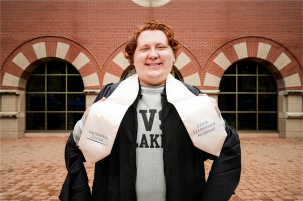 A person wearing a black graduation gown and a GVSU Lakers sweatshirt wears a scarf that says "Hauenstein Center" and "Cook Leadership Academy."
