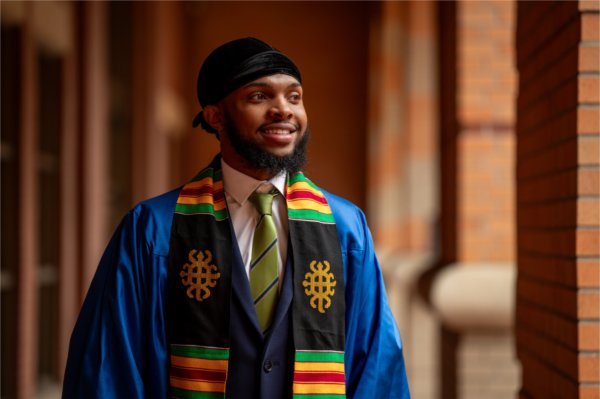 A person wearing a graduation robe, tie and scarf smiles in a posed photo.