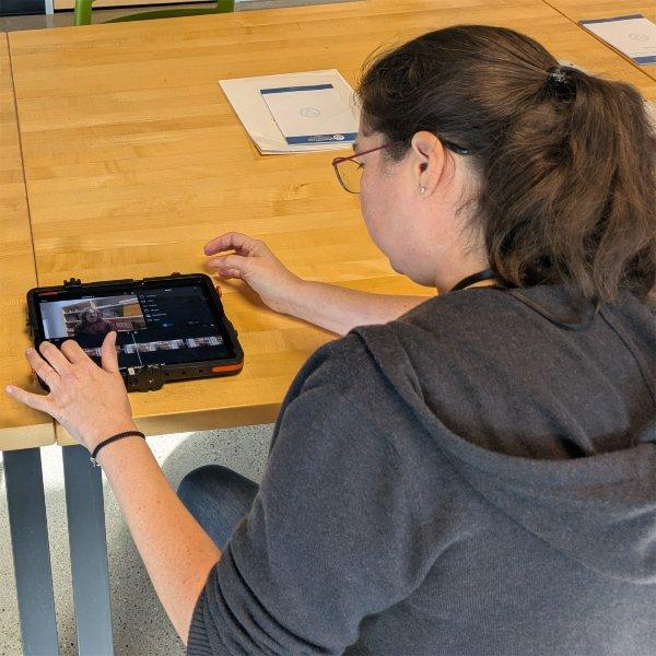 An educator reviews video-editing footage on a tablet during a workshop in a classroom.