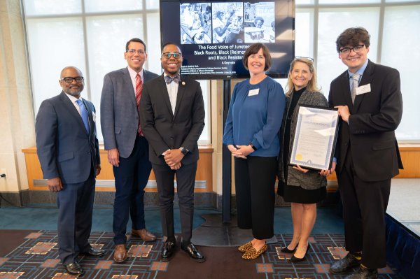 six people in front of a podium one person at right holding large framed certificate