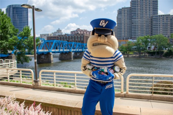 Louie the Laker holds a armful of canned goods while standing in front of the Grand River near the Eberhard Center