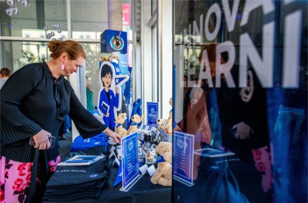 Maggie Lancaster in pink print pants and dark sweater looks at products on a display table