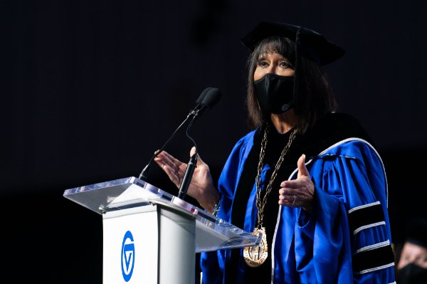 President Mantella in academic regalia gestures toward the audience from a podium