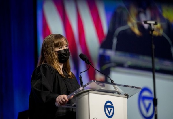 woman in graduation gown stands at podium