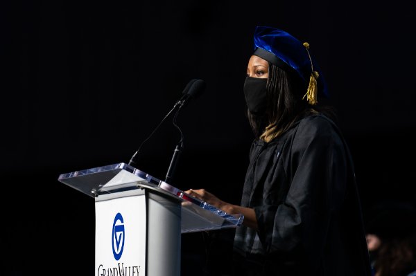 woman in academic regalia wearing face mask at podium