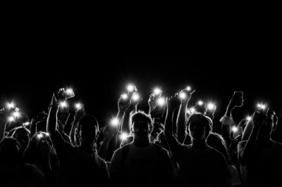 Silhouettes of people holding up phones with flashlights on. 