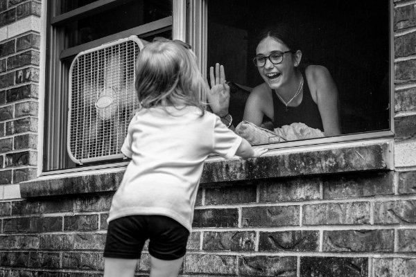 A child high-fives a person through a window screen, the person inside the window smiles.
