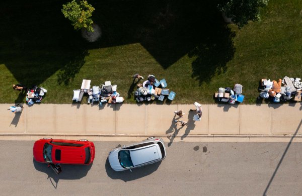  A bird's eye view of two cars parked along a sidewalk with several piles of belongings sitting in the grass.