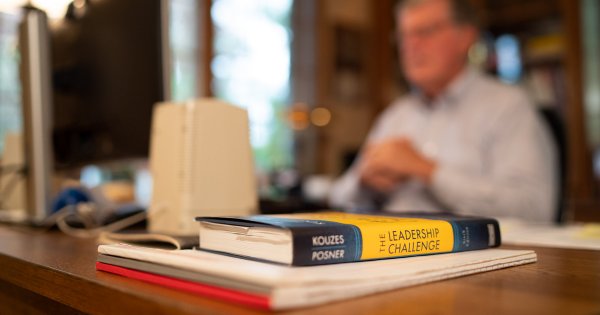 A blurred book in foreground, Haas sits in his home office teaching a class via Zoom.