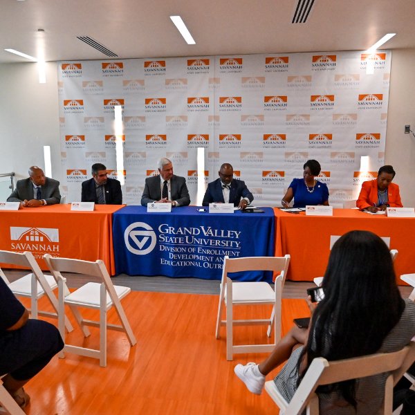 six people seated at table signing papers, with table drapes of savannah state university and GVSU