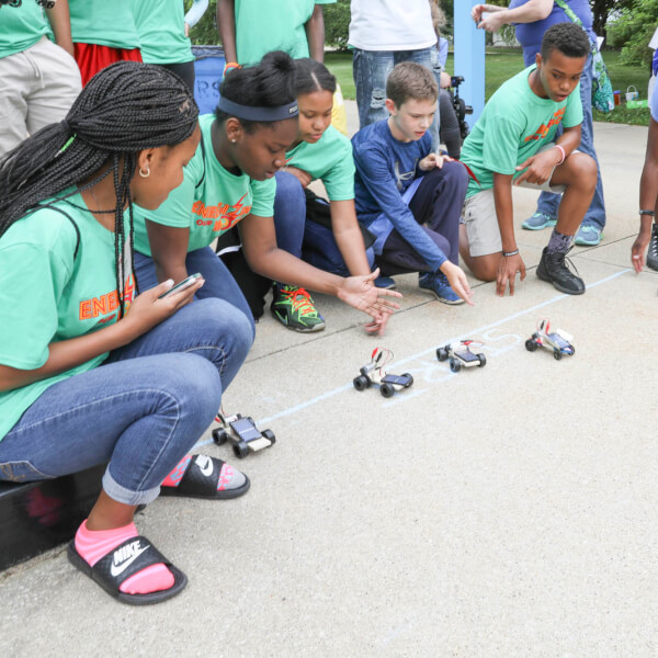 Campers racing their solar-powered cars under the Transformational Link sculpture.