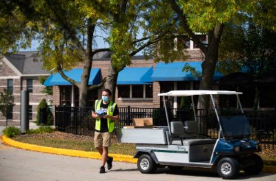 A male GVSU student and Laker Outreach Ambassador wearing a bright yellow vest walks toward other students on the Allendale Campus.