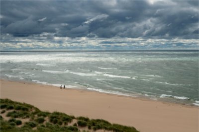 Two people are seen from a distance walking along Lake Michigan on a cloudy day.