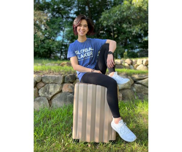 Aliah Lloyd, senior majoring in computer science, is pictured sitting on a suitcase with a Global Lakers tshirt on