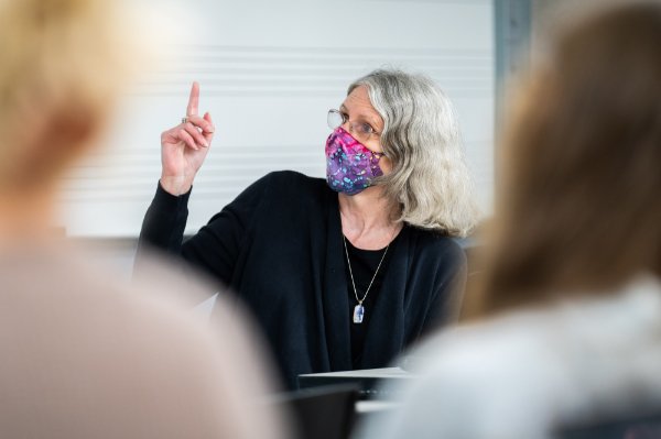 Karen Gipson, seated, points to the white board. She is wearing a face mask in class.