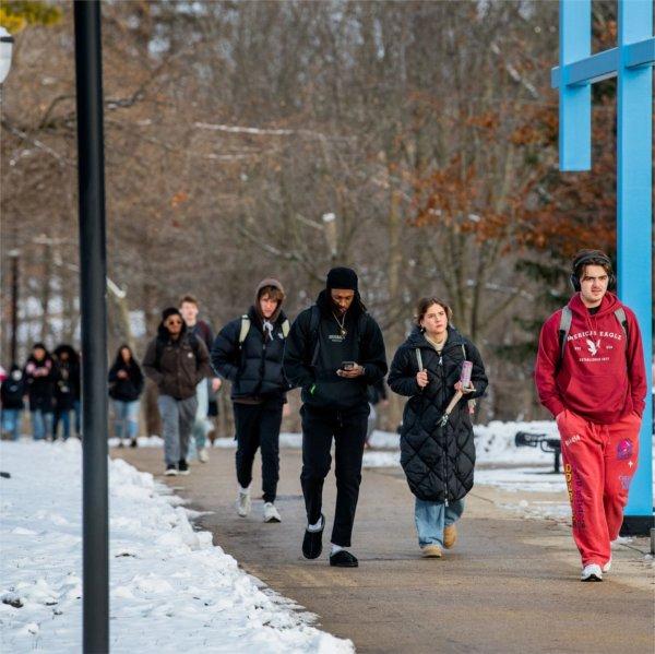 students walking under the blue artwork called the Transformational Link, light snow on the ground