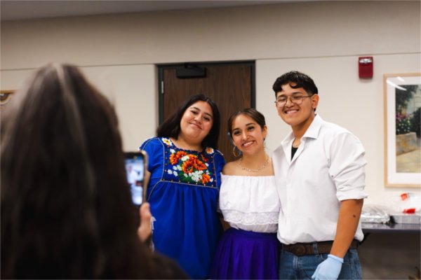 Three students smile for a photo before helping serve dinner.