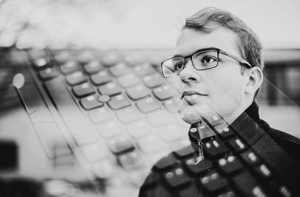 student with glasses, computer keyboard superimposed over his face