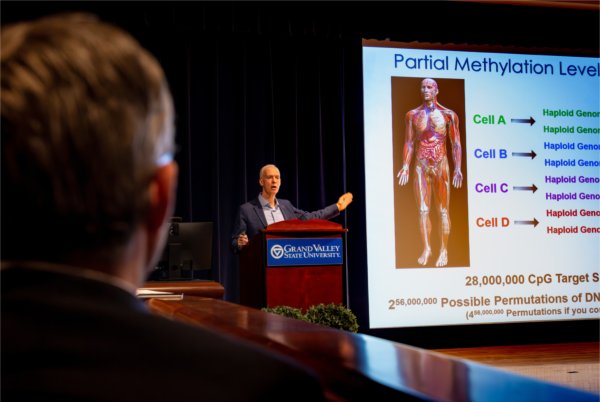 A man stands a lectern delivering a presentation on artificial intelligence and medical research.