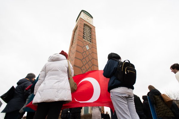 Two people hold a red and white flag while standing in front of the carillon.